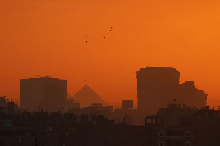 Silhouette buildings in city against orange sky