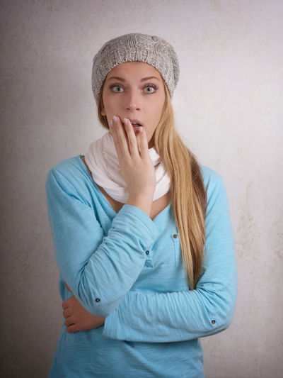 Portrait of shocked young woman standing against wall