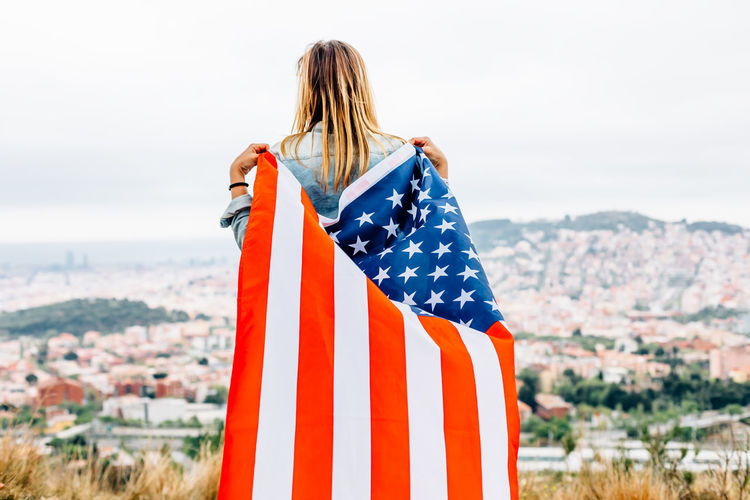 Rear view of woman with american flag standing against the sky