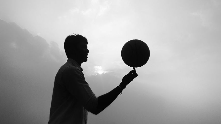 Side view of man holding balloons against sky