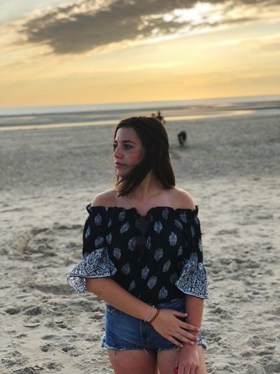 Thoughtful teenage girl standing at beach during sunset