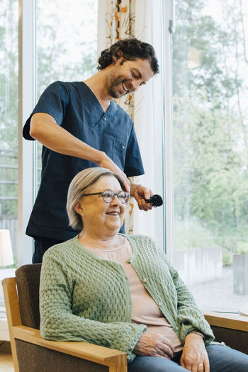 Smiling male nurse brushing senior woman's hair at retirement home