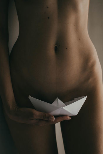 Midsection of woman holding paper boat against body