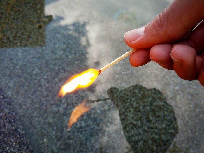 Cropped image of hand holding burning matchstick