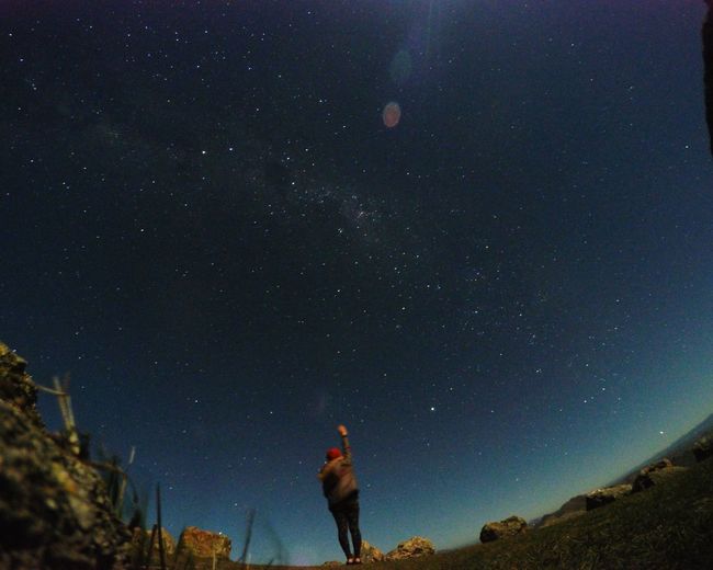 Rear view of person standing with arm raised against starry sky