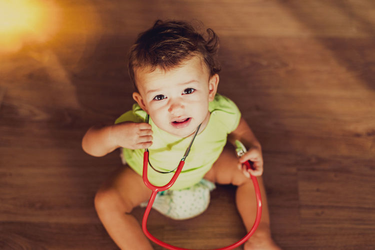 Portrait of cute baby girl with stethoscope sitting on hardwood floor