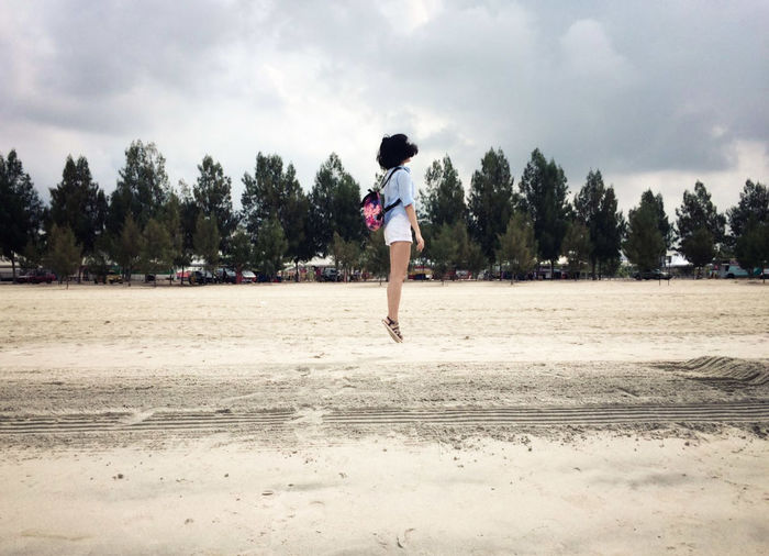 Full length of woman jumping over beach against cloudy sky