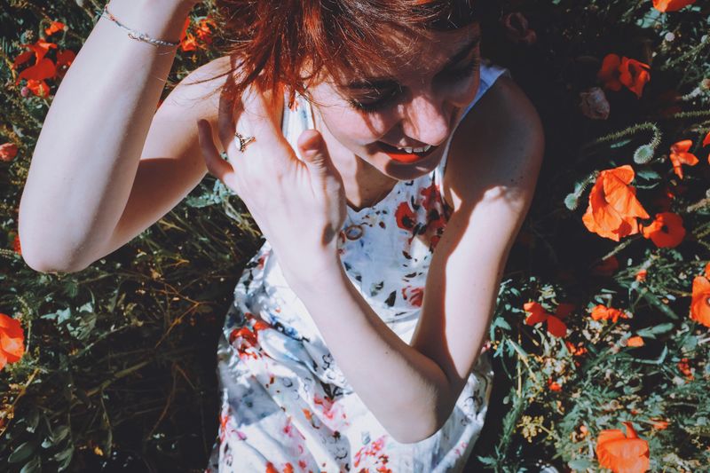 High angle view of cheerful woman lying amidst orange poppy field