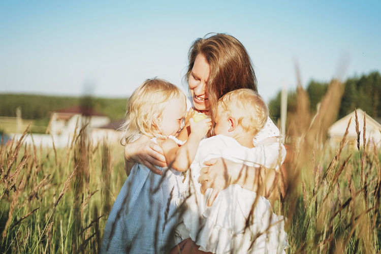 Young woman mom with baby girls twins on hands hug in backyard of cottage in sunset light