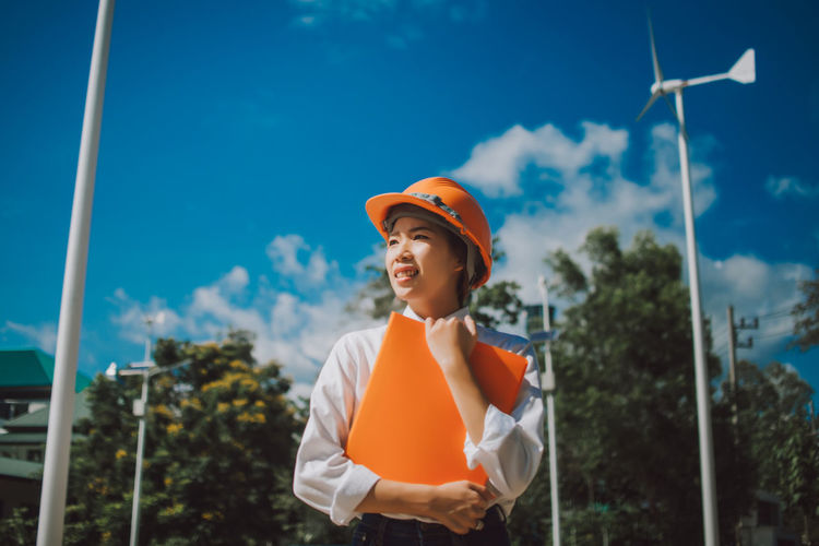 Low angle view of female engineer standing against windmill