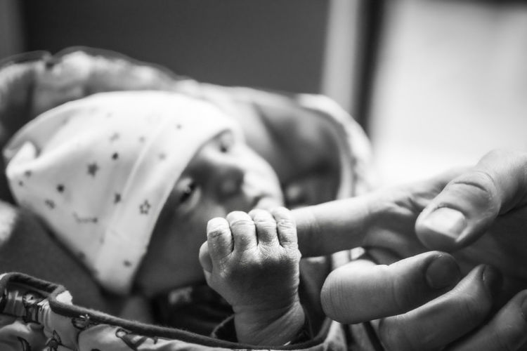Newborn baby holding father's finger. defocused background. black and white edit.