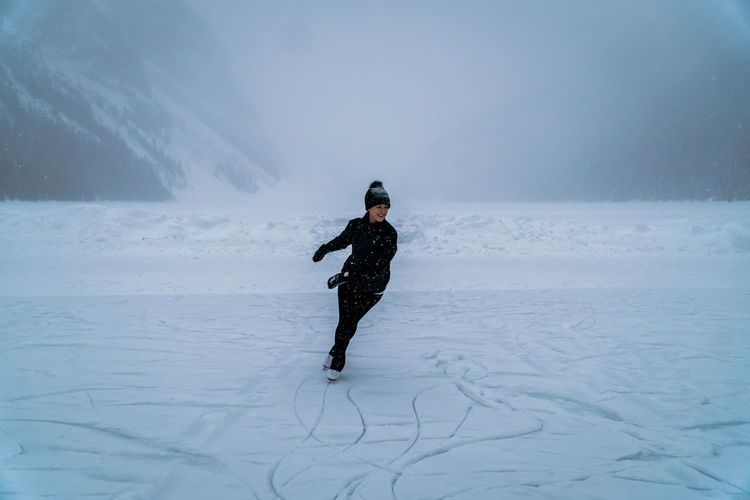 Female ice skater skating on frozen lake outside in snowstorm near forest in canada.