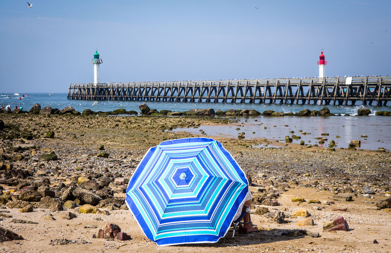 View of umbrella on coast against pier in sea