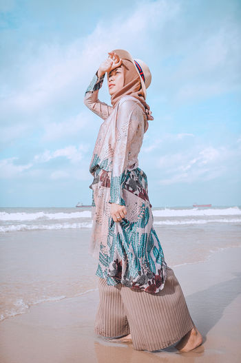 Full length of woman looking away while standing on beach against sky