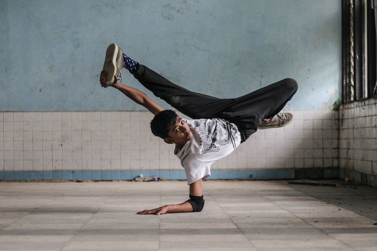 Portrait of young man performing stunts in room against wall