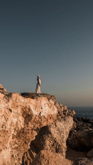 Distant view of woman standing by cliff against sky