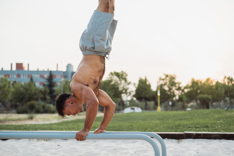 Side view of fit hispanic ethnic male athlete performing handstand on parallel bars while doing exercises during calisthenics training on the street