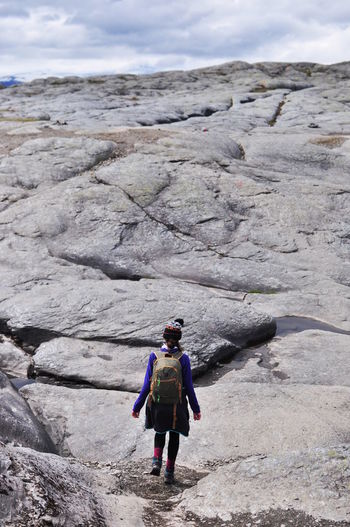 Rear view of backpack woman walking on rock formation