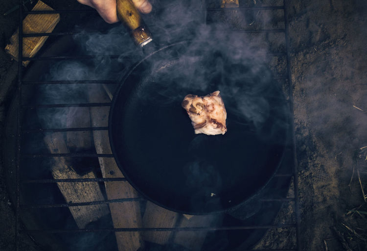 Cropped hand frying meat on wood burning stone