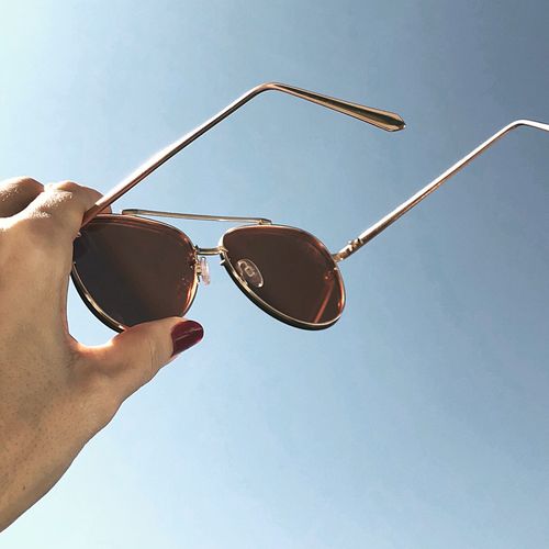 Low angle view of hand holding sunglasses against clear sky