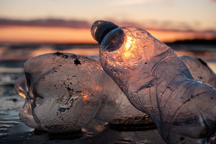 Close-up of rusty bottle on beach against sky during sunset