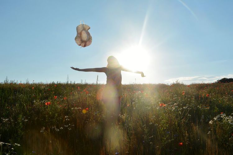 Happy girl with flying hat in a poppy meadow in sunlight