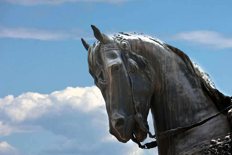 Low angle view of bronze horse statue against sky