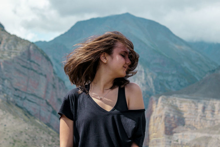 Young woman tossing her hair standing against mountain range