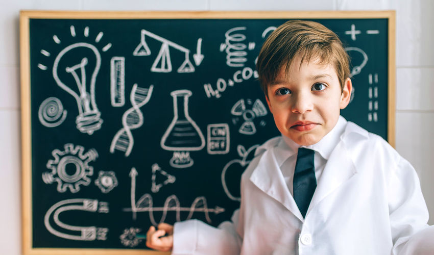 Portrait of cute boy standing against blackboard in classroom
