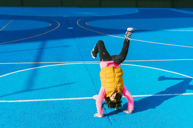 Playful girl practicing handstand on soccer court