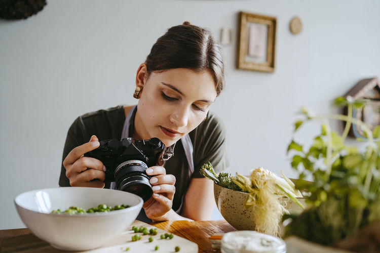 Food stylist adjusting camera lens while photographing green peas in studio
