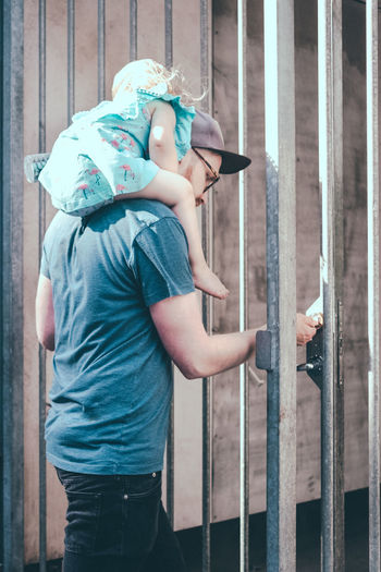 Rear view of man opening gate while carrying daughter on shoulders