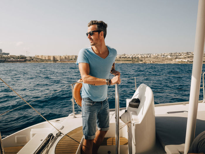Mature man wearing sunglasses sailing boat in sea against sky
