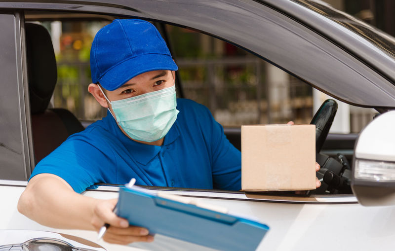 Young man wearing mask holding clipboard while sitting in car