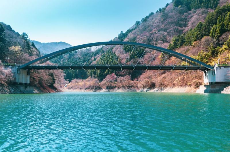 View of tied-arch bridge that crosses over a river feeding into okutama lake reservoir.