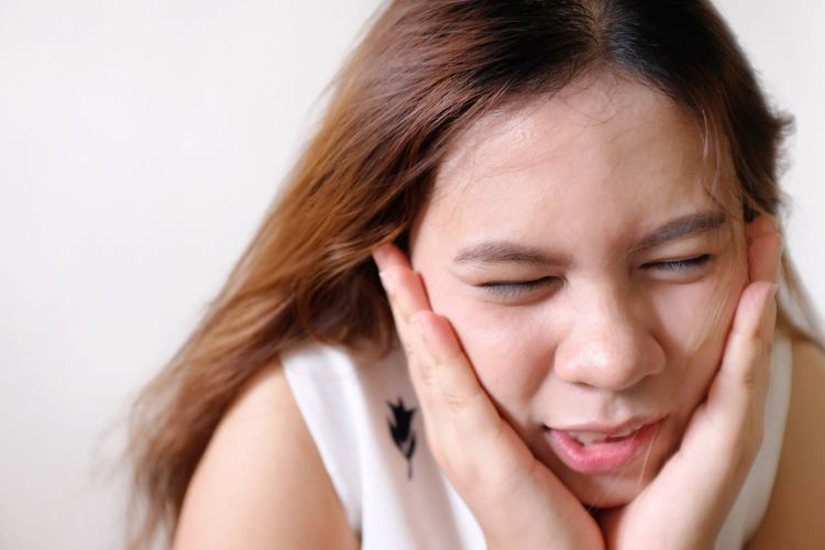 Young woman suffering from toothache against white wall