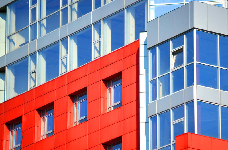Part of the facade of a modern building with red walls, square windows, the blue mirrored glass. 