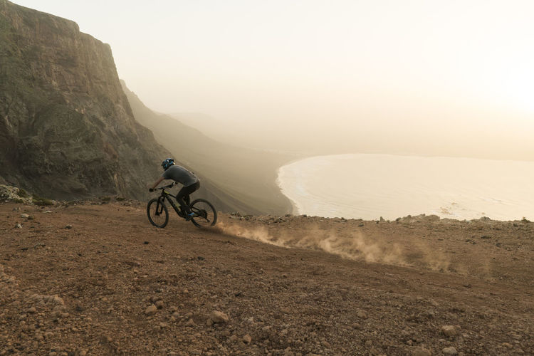 Spain, lanzarote, mountainbiker on a trip at the coast at sunset