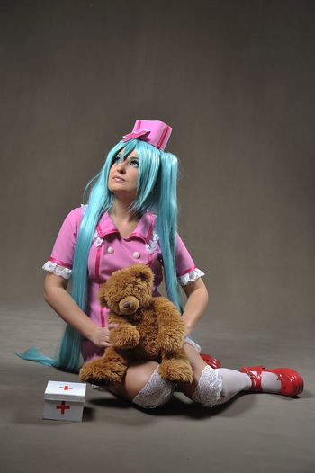Young nurses with long blue hair holding teddy bear against gray background