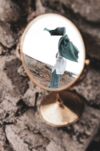 Close-up of hand mirror with reflecting woman standing against sky