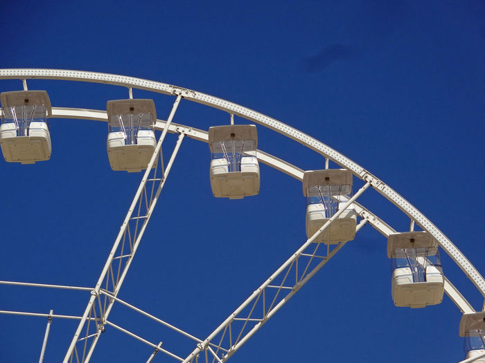 Low angle view of ferris wheel against clear blue sky on sunny day