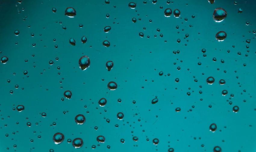Full frame shot of water drops on glass against blue sky