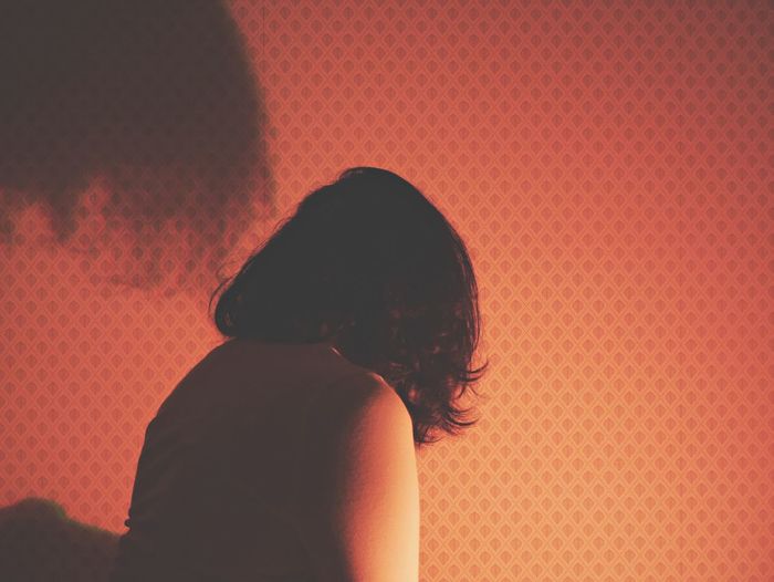 Rear view of depressed woman by wall in illuminated room