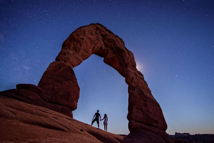 Low angle view of couple standing at arches national park during sunset
