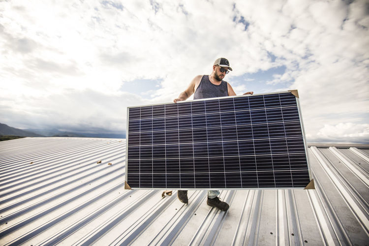 Man carrying solar panel on roof during installation.