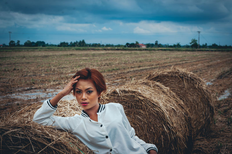 Portrait of woman sitting on hay bale at field
