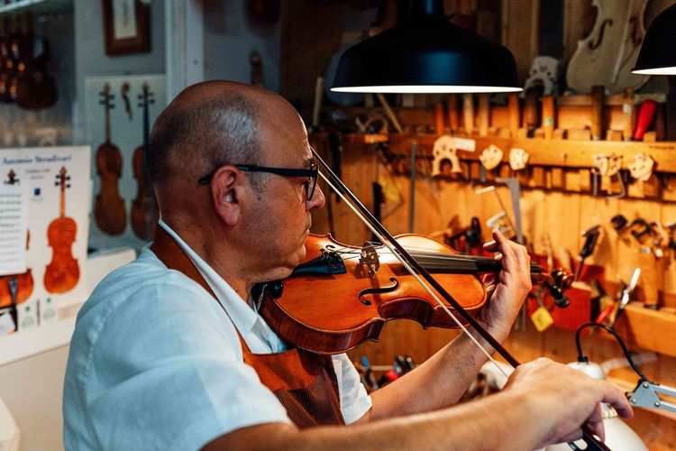 Side view of mature male artisan luthier testing violin after restoration in workshop