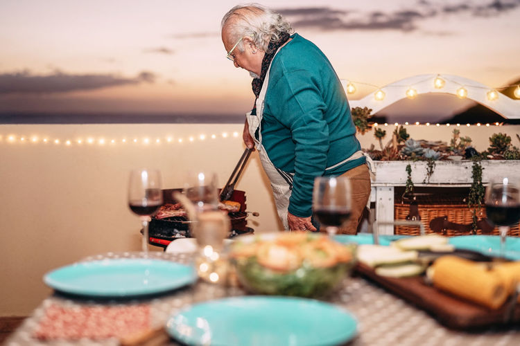 Man preparing food on table against sky during sunset