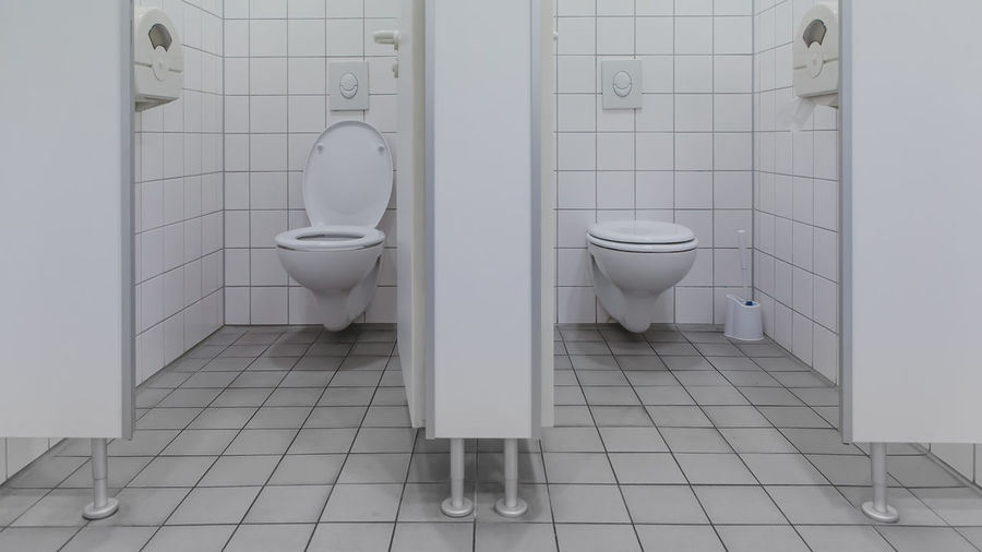 Separated toilets at public restroom beside white cabins and open and closed wc