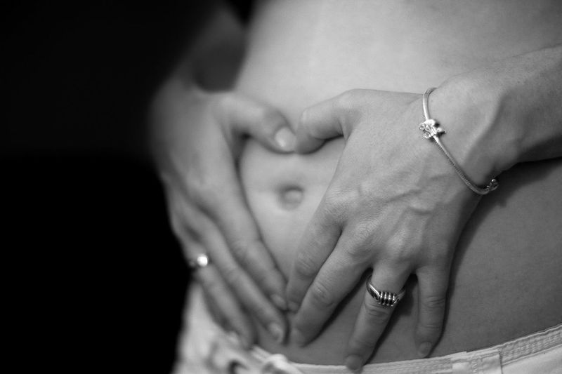 Midsection of shirtless pregnant woman touching her belly